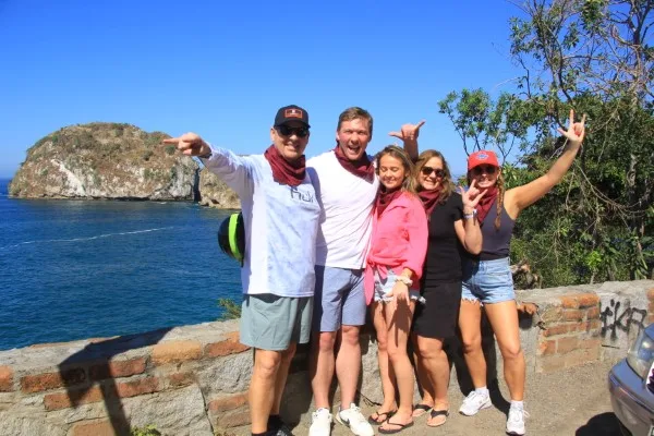  Family posing for a photo with a beach in the background in Puerto Vallarta; unique things to do in Puerto Vallarta.