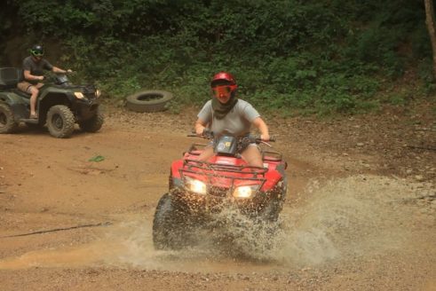 Persona Conduciendo Una ATV Mientras Cruza Un Río, Destacando La Habilidad Del Vehículo Para Terrenos Complicados Y Llenos De Agua.